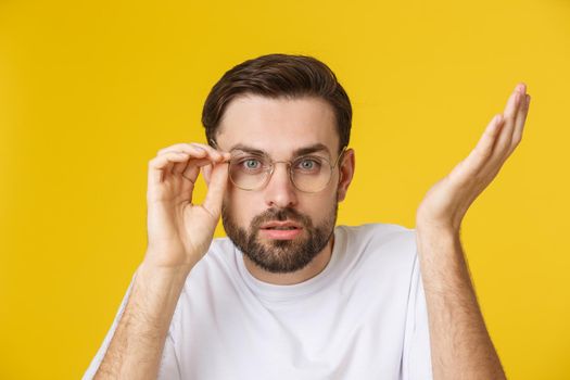 Closeup of young handsome man looking and showing funny face at camera, wearing glass. Isolated view on yellow background
