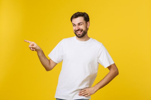 Man pointing showing copy space isolated on yellow background. Casual handsome Caucasian young man