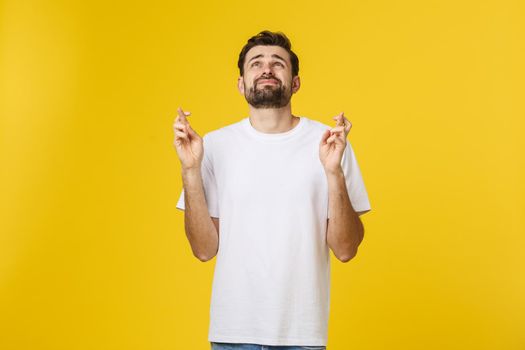 Young man making a wish isolated on yellow background.