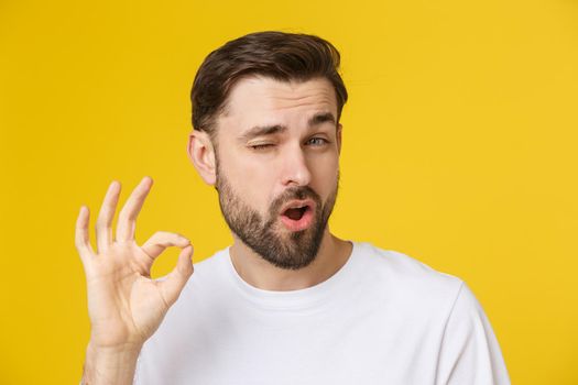 Satisfied young man showing okay sign isolated on yellow background