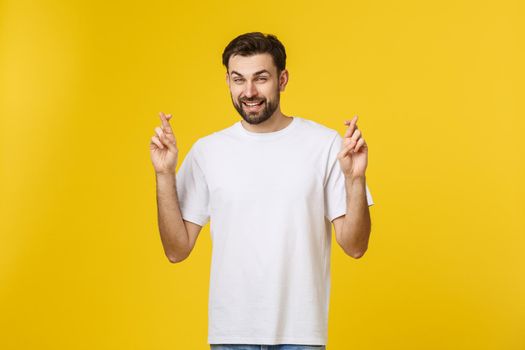 Young man making a wish isolated on yellow background.