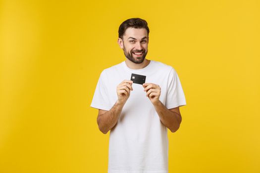 Happy smiling young man showing credit card isolated on yellow background.