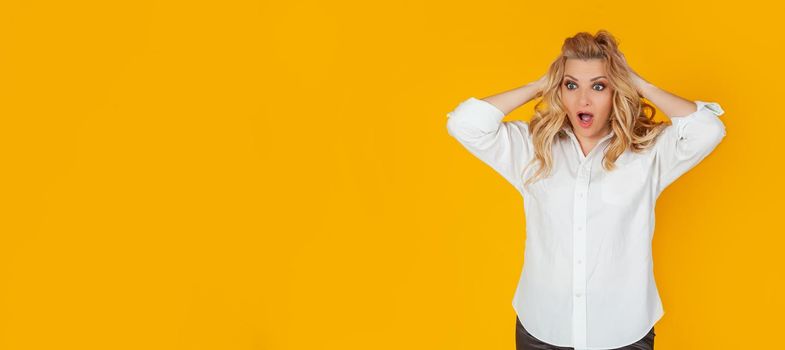 Portrait of a woman in a panic with her hands clutching her head, excited and looking panicky down, hands clutching her head, breaking an expensive thing, alarmed indecisive, on a yellow background