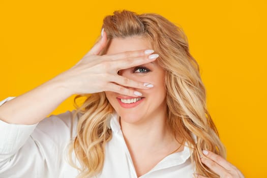 Portrait of a beautiful enthusiastic woman with curly blond hair closes her eyes and looks through her fingers, smiling. Looking to the future with an optimistic look.