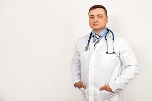 Portrait of smiling young male doctor with a stethoscope around neck standing within a white coat, isolated on gray background