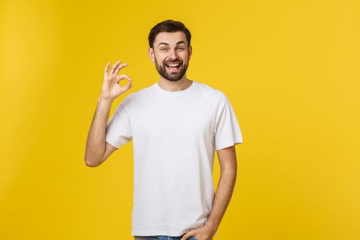 Portrait of a cheerful young man showing okay gesture isolated on yellow background.