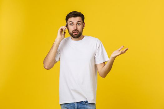 Portrait of a serious man talking on the phone isolated on a yellow background. Looking at camera.