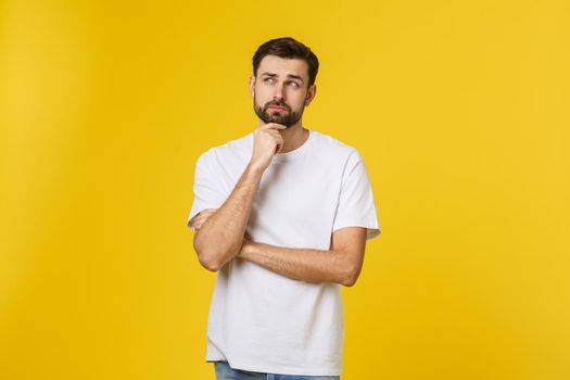 Pensive curious man looking up in thinking pose trying to make choice or decision isolated on yellow background