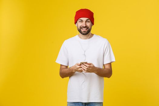 Dance. Handsome young stylish man in headphones holding mobile phone and dancing while standing against yellow background.