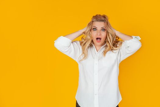Portrait of a woman in a panic with her hands clutching her head, excited and looking panicky down, hands clutching her head, breaking an expensive thing, alarmed indecisive, on a yellow background