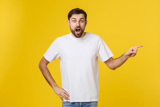 Man pointing showing copy space isolated on yellow background. Casual handsome Caucasian young man