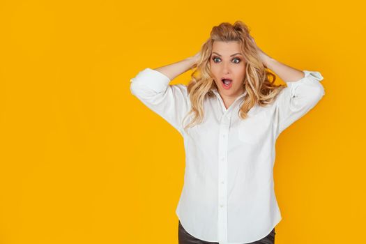 Portrait of a woman in a panic with her hands clutching her head, excited and looking panicky down, hands clutching her head, breaking an expensive thing, alarmed indecisive, on a yellow background