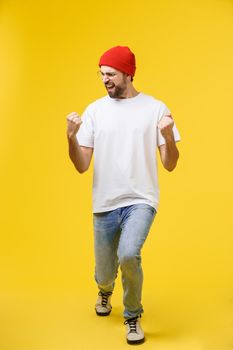 Happy young man with arms up isolated on a yellow background