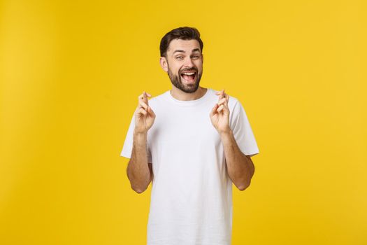 Young man making a wish isolated on yellow background.