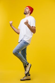 Happy young man with arms up isolated on a yellow background