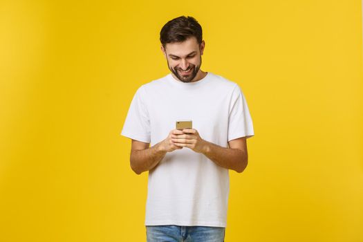 Good news from friend. Confident young handsome man in jeans shirt holding smart phone against yellow background.