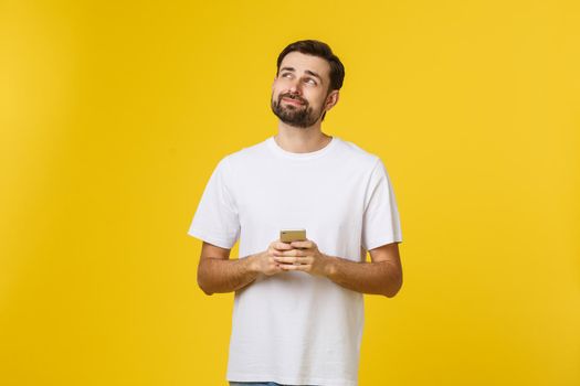 Good news from friend. Confident young handsome man in jeans shirt holding smart phone against yellow background.