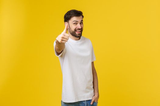 Young happy man with thumbs up sign in casuals isolated on yellow background.