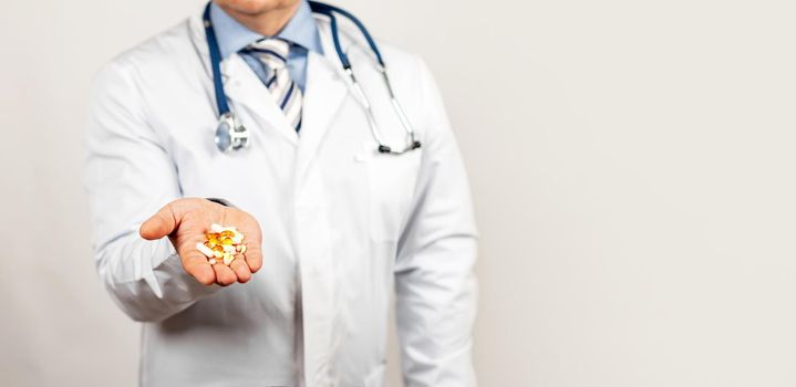 A doctor in a medical coat holds pills and capsules on the palm of his hand. A prescription for treatment with a drug A male doctor suggests taking medicine for health or an antibiotic and painkiller.