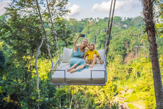 Mother and son swinging in the jungle rainforest of Bali island, Indonesia. Swing in the tropics. Swings - trend of Bali. Traveling with kids concept. What to do with children. Child friendly place.