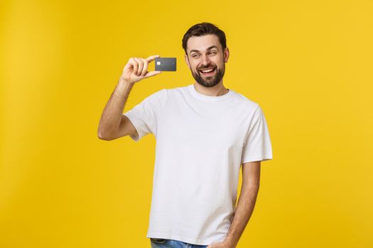 Happy smiling young man showing credit card isolated on yellow background.