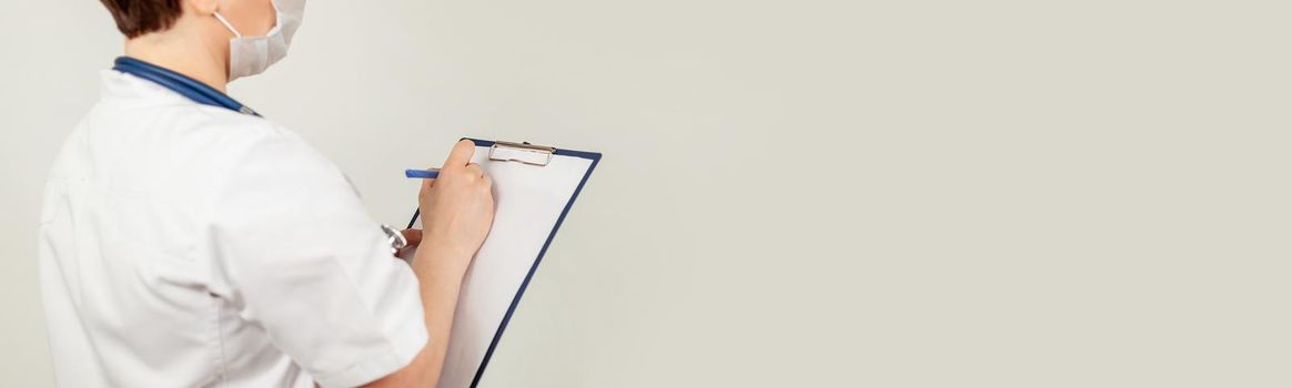 Female doctor writes with a pen a document on a tablet, writes a medical history. The concept of healthcare, medicine and pharmacy.