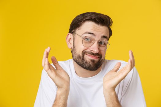 Closeup of young handsome man looking and showing funny face at camera, wearing glass. Isolated view on yellow background