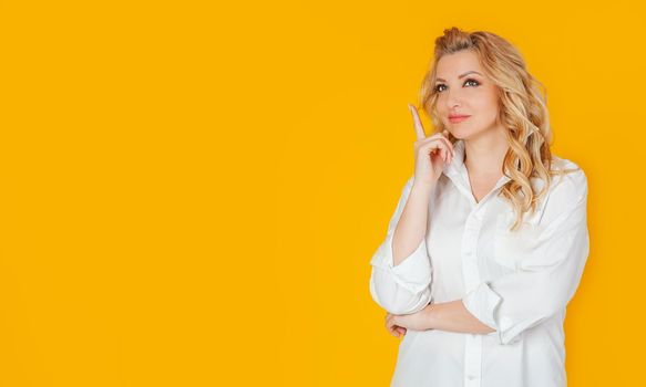 Young pretty girl holding a finger up having a good idea, pointing with a finger, happy smiling woman having an idea on yellow background. Copy space template