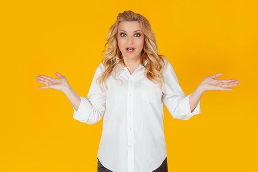 A clumsy European blonde woman in a white shirt, shrugging her shoulders to the sides, not suspecting, asks, perplexed, uncertain expression on her face, ignorant to say, Oh, sorry, I didn't know.