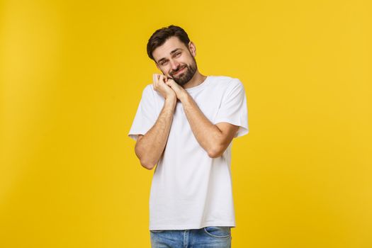 Young man looks to the camera and smiles shy. He's got his hands on cheek. Isolated, with a beard and a white T-shirt.