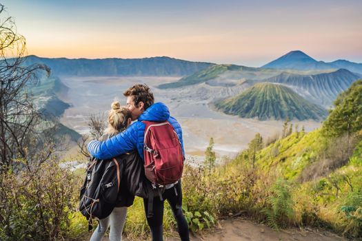 Young couple man and woman meet the sunrise at the Bromo Tengger Semeru National Park on the Java Island, Indonesia. They enjoy magnificent view on the Bromo or Gunung Bromo on Indonesian, Semeru and other volcanoes located inside of the Sea of Sand within the Tengger Caldera. One of the most famous volcanic objects in the world. Travel to Indonesia concept.