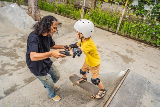 Athletic boy learns to skateboard with asian trainer in a skate park. Children education, sports. Race diversity.