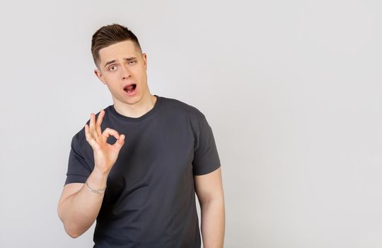 Handsome, confident young man guaranteeing impeccable quality, shows a well-confirming gesture, smiles, satisfied, approves a good idea, recommends a promo agrees with you stands on a white background