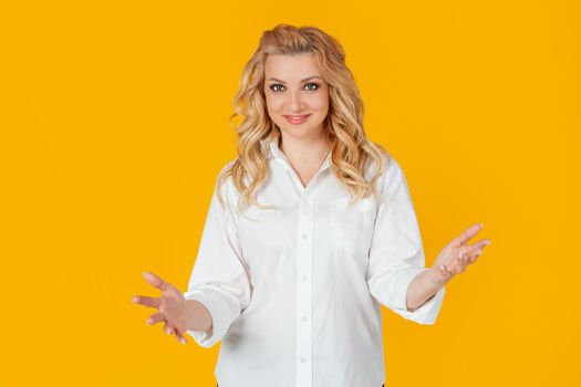 Sociable cute woman in white shirt, middle aged European girl, extends her arms to the camera in greeting and warm welcome, wanting to hug or hug, standing against yellow background.