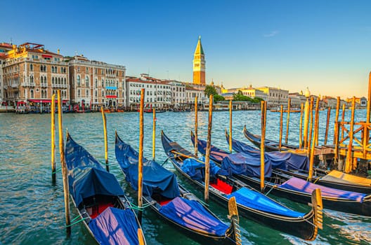 Gondolas moored in water of Grand Canal waterway in Venice. Baroque style colorful buildings along Canal Grande and bell tower Campanile di San Marco. Typical Venice cityscape, Veneto Region, Italy