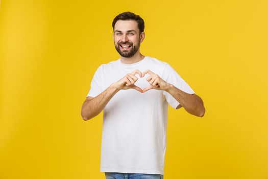 smiling young boy making heart gesture on his chest with white shirt isolated on yellow background.
