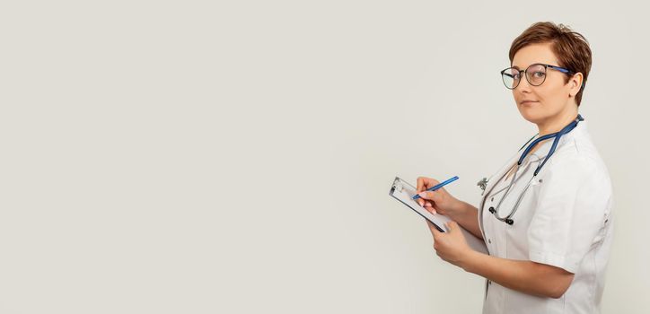 Female doctor writes with a pen a document on a tablet, writes a medical history. The concept of healthcare, medicine and pharmacy.