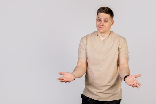 Beautiful young guy a man smiles and shrugs spreading hands, does not know what to say in response. Language of the body. Looks at the camera.