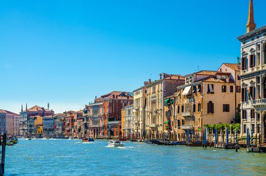 Venice cityscape with Grand Canal waterway, Venetian architecture colorful buildings, wooden pier, yacht boats sailing Canal Grande, blue sky in sunny summer day. Veneto Region, Northern Italy.