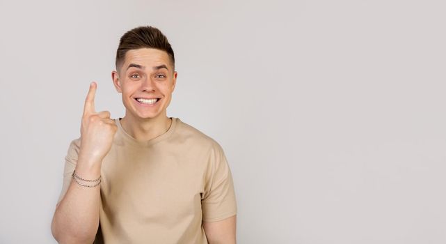Portrait of a cheerful guy pointing fingers up, showing number one, smiling carefree, giving advice, advertising a product, indicating which link to click, white background