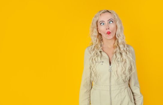 Amusing, playful cute woman, showing her cheerful side, playing charades, imitating fish, folding her lips and squinting, turning her eyes, standing on a yellow background, cheerfully grimacing