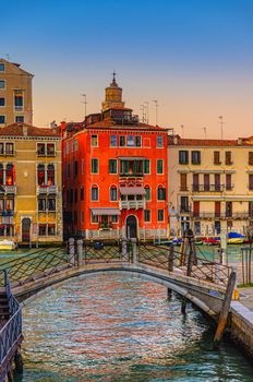 Bridge across narrow water canal and baroque style buildings palaces on Grand Canal waterway in Venice historical city centre San Marco sestiere, sunset evening view, Veneto Region, Northern Italy
