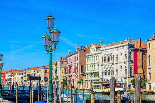 Pier dock with wooden poles of Grand Canal waterway in Venice historical city centre with row of colorful buildings Venetian architecture, seagulls in blue sky. Veneto Region, Northern Italy.