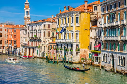 Grand Canal waterway in Venice historical city centre with sailing gondola, Palazzo Civran palace, colorful buildings and Church Holy Apostles of Christ bell tower. Veneto Region, Northern Italy.