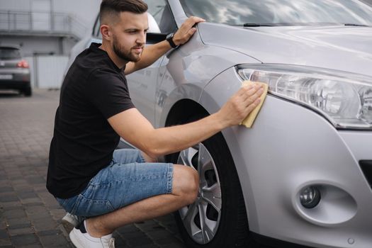 Hand of man wipes headlight of his car using rug. Self-service car wash. Outdoor.