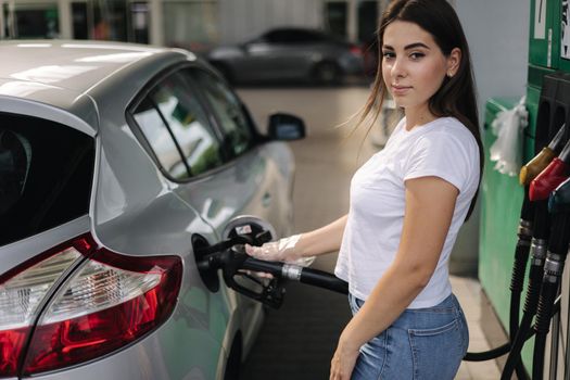 Attractive young woman refueling car at gas station. Female filling diesel at gasoline fuel in car using a fuel nozzle. Petrol concept. Side view.