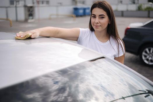 Woman wipes a windshield of his car with a rag in a showroom at a self-service car wash.