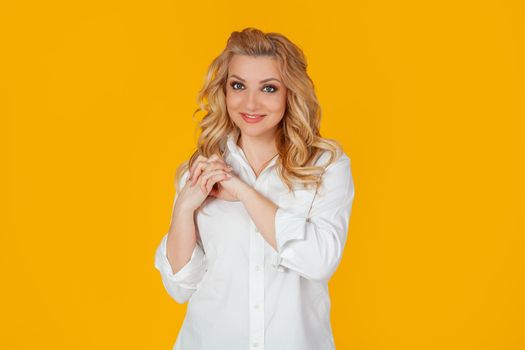 Woman in white shirt, middle-aged European lady, palms together are grateful, appreciate a pretty good gift with gratitude, look romantic, appreciate kindness, stands on yellow background.