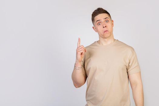 A handsome guy with a beautiful haircut looks at the camera with a funny facial expression, holding his lips and pointing his finger up. Copy space