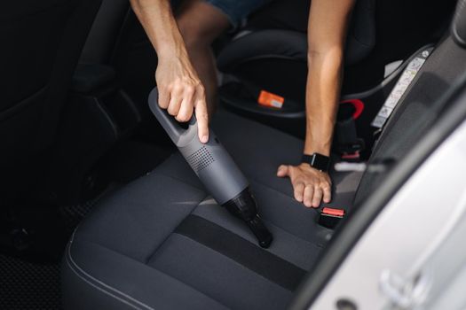 Close up of male using portable vacuum cleaner in her car. Electrical vacuum in man's hand clean car inside from dust.